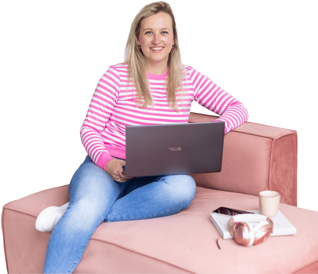 Vrouw met een laptop zit op een roze bank, gekleed in een gestreepte trui en spijkerbroek. Naast haar staan een kopje koffie en een smartphone, wat een ontspannen werkomgeving uitstraalt.