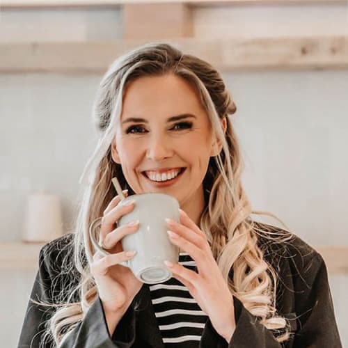 Vrouwelijke barista met een glimlach die een kopje koffie vasthoudt in een moderne café-omgeving. Haar lange, golvende haar en stijlvolle outfit dragen bij aan een warme en uitnodigende sfeer.